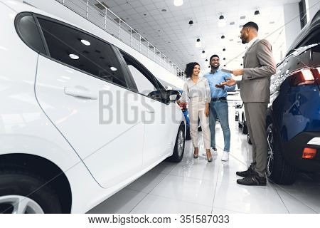 Car Sales. African American Spouses Buying New Car Choosing Auto With Seller Man In Luxury Automobil