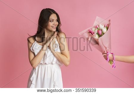 Flowers Delivery Service. Hand Giving Bouquet Of Tulips To Surprised Girl, Pink Stusio Background, C