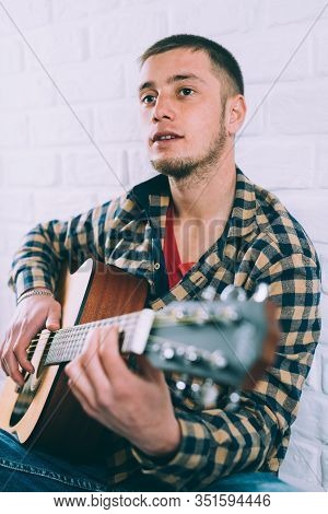 Handsome Mature Man In Casual Clothes Is Smiling While Playing Guitar At Home