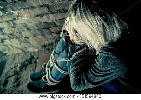 Blonde Girl With Bound Hands And Feet Is Sitting In The Basement, Covering Her Face With Her Hands A
