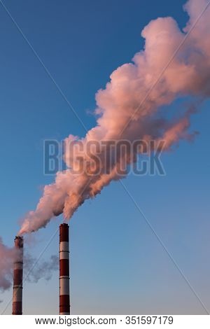 Two Pipes Of A Boiler Room With Thick Pink Smoke At Sunset. Beautiful Pink Steam, Clear Blue Sky. Ai