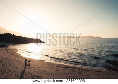 Woman And Dog Walk Along The Golden Plage De Sainte Restitude Beach At Sunset In The Balagne Region 