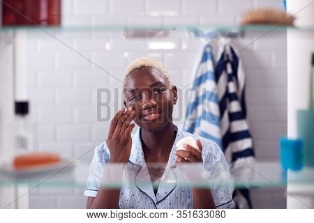 View Through Bathroom Cabinet Of Woman Getting Ready For Work And Moisturizing Skin