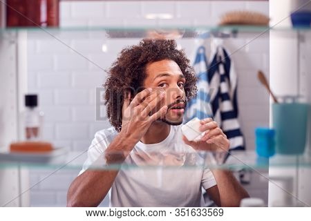 View Through Bathroom Cabinet Of Man Getting Ready For Work And Moisturizing Skin