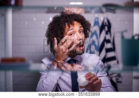 View Through Bathroom Cabinet Of Young Businessman Getting Ready For Work And Moisturizing Skin