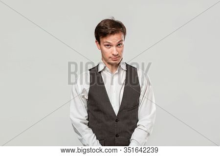 Young Man In A White Shirt And Grey Vest In High Dudgeon Over Grey Background.