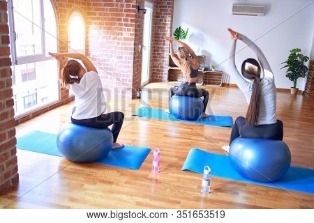 Young beautiful group of sportswomen practicing yoga. Stretching using fitness ball at gym