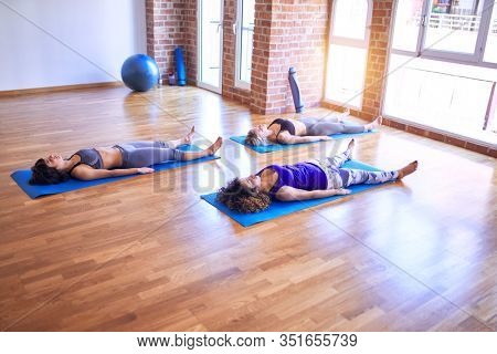Young beautiful group of sportswomen practicing yoga. Lying down doing corpse pose at gym