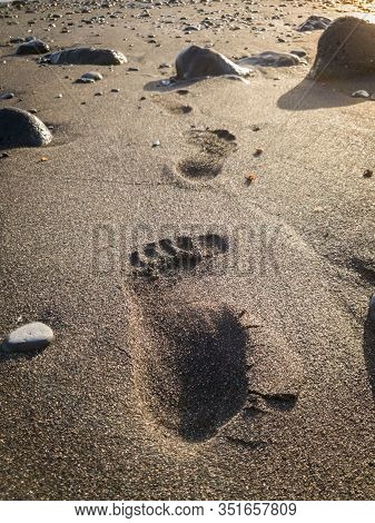 Closeup Image Of Male Footrpint On The Black Sand On The Beach At Sunset