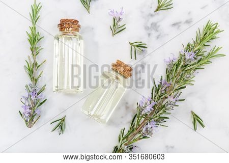 Rosemary Essential Oil In Glass Bottle And Twigs On Marble Table. Salvia Rosmarinus Oil. Top View