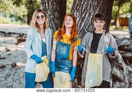 Friends Picking Up Trash From The Park. They Collecting The Litter In Garbage Bag