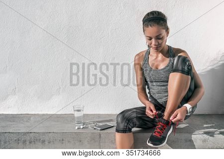 Runner woman tying running shoes laces wearing tech wearable technology smartwatch. Female athlete jogger using smart phone living a healthy active lifestyle drinking water.