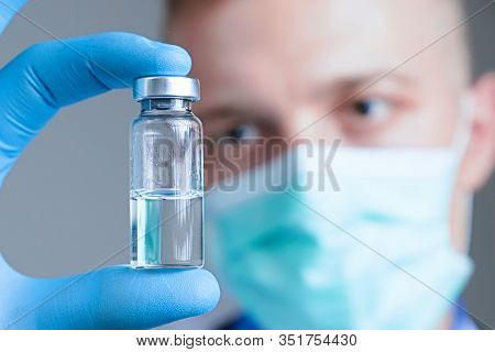 Close Up Hand Of Doctor In Blue Latex Glove And Medical Gauze Mask With Glass Ampoule. Health And Va
