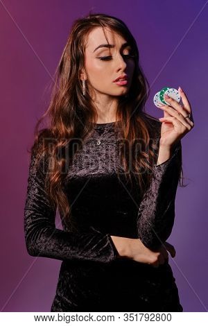 Brunette Woman In Black Velvet Dress Showing Multicolored Chips, Posing Against Coloful Background. 