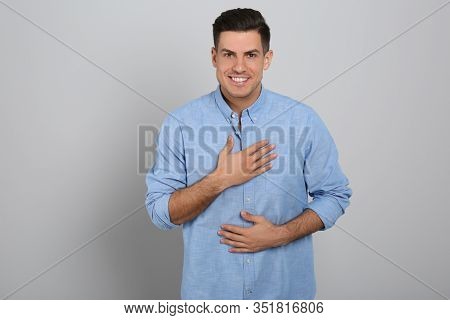 Handsome Grateful Man With Hands On Chest Against Light Grey Background