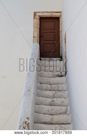 White Facade Of The Church Igreja Matriz De Alvor. Old Stairs To A Brown Wooden Closed Door With Sto