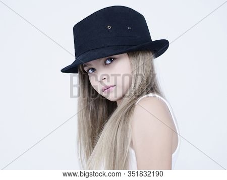 little pretty girl in black classic hat. Studio ashion photography of kid in white dress. Beautiul model on white background.