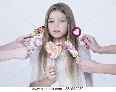 little pretty girl with big candy. Studio ashion photography of kid in white dress. Beautiul model eating sweet lollipop.