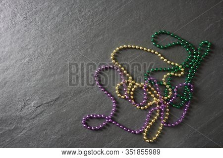 Purple, Green And Gold Mardi Gras Beads On A Gray Slate Table With Copy Space