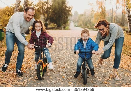 Caucasian Family Helping Their Kids To Ride The Bike Pushing Them And Make Feel Safe
