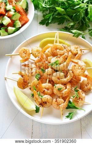 Grilled Shrimp Skewers. Prawns Skewers With Greens, Spices And Lemon On White Plate Over Wooden Tabl