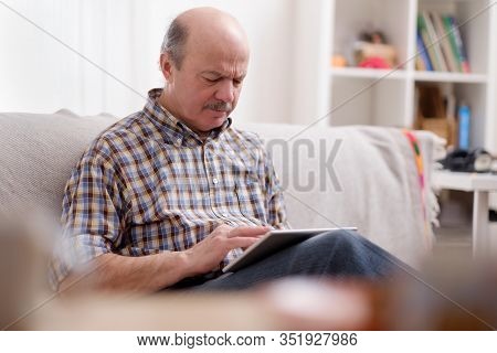 Handsome Seniorman Using A Tablet At Home Sitting On A Sofa