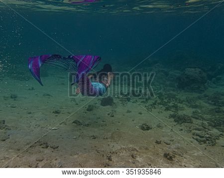 Young Female Free Diver Swims Underwater In A Colorful And Sexy Mermaid Costume.