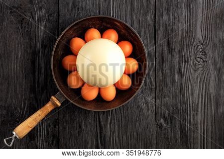 Ostrich Egg Surrounded By Chicken Eggs In An Old Cast-iron Skillet, Which Is Standing On An Old Blac