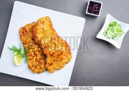 Traditional deep fried Wiener schnitzel from veal topside with cucumber salad and cranberry jam offered as top view on a modern design plate on a rustic wooden board 