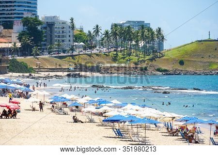 People Enjoying Sun, Beach And Blue Water At Porto Da Barra Beach Next The Barra Lighthouse In Salva