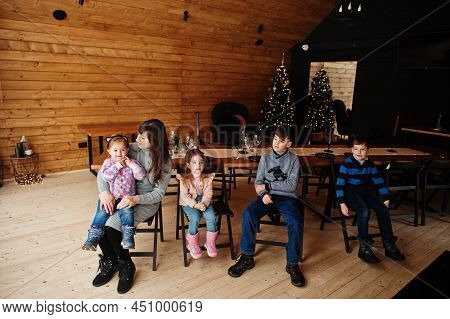 Mother And Kids In Modern Wooden House Sitting Against Table With Christmas Tree, Spending Time Toge