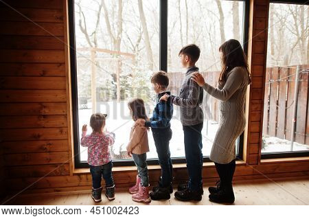Mother And Four Kids In Modern Wooden House Against Large Window.