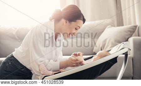 Happy Mother Playing With Girl Baby Lies In Automatic Carrycot, Sunlight At Home