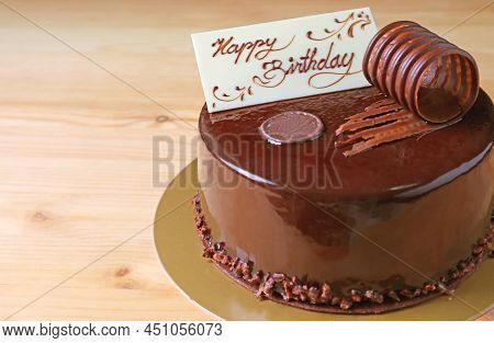 Delectable Chocolate Cake Topped With Creamy White Edible Birthday Greeting Card On Wooden Backdrop