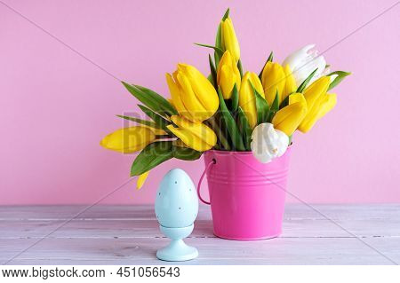 Easter Holiday Decorations: Wooden Egg And Bouquet Of Yellow Tulips In Bucket On Pink Background. Co