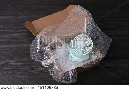 Small Fan With Bubble Wrap And Packaging Foam In Cardboard Box On Dark Wooden Table