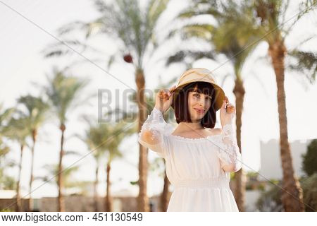 Lovely Smiling Lady With Red Hair Posing With Hand Up Touching Strow Hat Standing On Blur Background