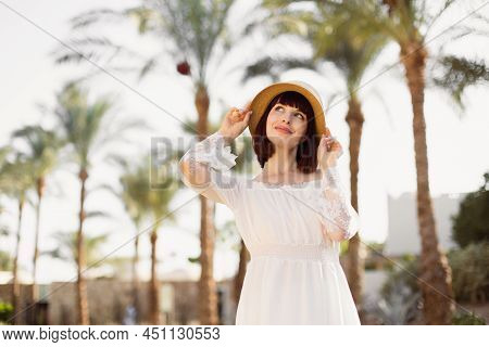 Lovely Smiling Lady With Red Hair Posing With Hand Up Touching Strow Hat Standing On Blur Background