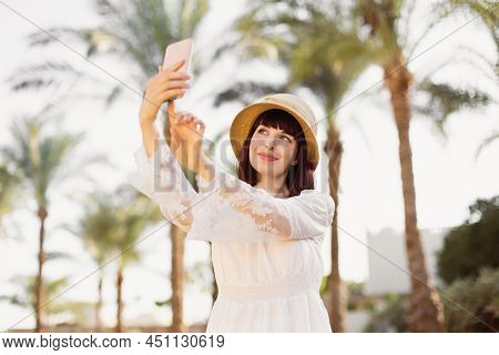A Woman In Srtaw Hat And White Dress Using Smart Phone Or Taking A Selfie On The Background With Pal
