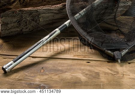 Fishing Landing Net On A Wooden Background. Fishing Net And Fishing Rod Near The Tree. View From Abo