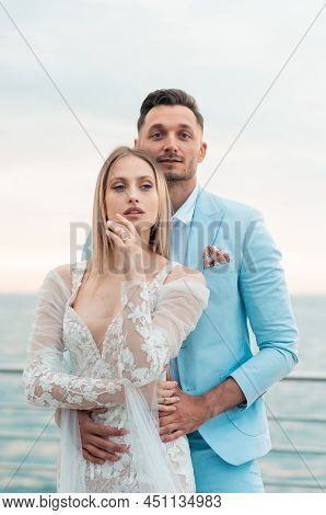 Young Bride, Fashionable, Blonde Model In Luxury Wedding Dress With Groom On The Coast. Girl In Long