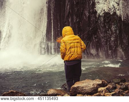 A Woman Blown By The Wind Takes A Step Into A Mountain River Into Which A Powerful Icy Stream Of A W
