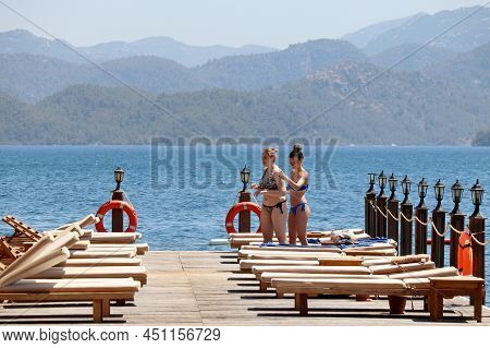 Hisaronu, Turkey - July 2021: Two Happy Girls Apply Sunscreen To Each Other On A Beach On Mountains 