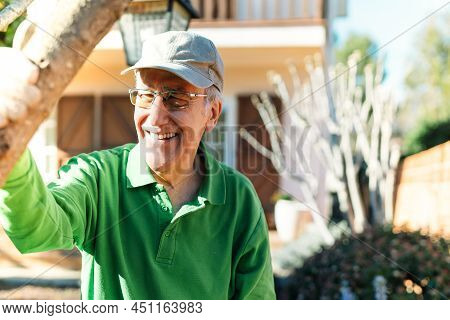 Portrait Of An Elderly Man Leaning On The Branch Of A Tree In His Garden