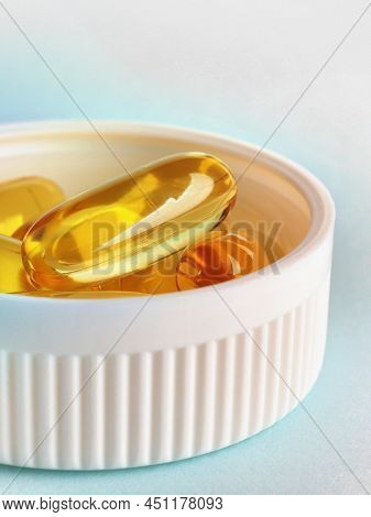 Fish Oil. Yellow Softgels Or Capsules Are In Bottle Cap. Blue And White Surface. Vitamins And Health