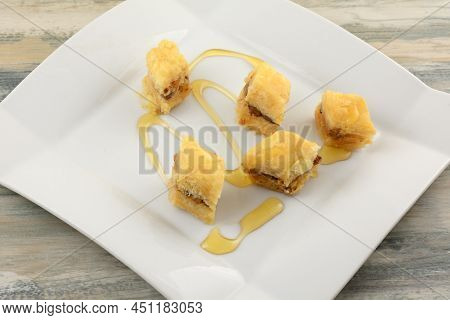Pieces Of Nut Baklava With Honey On White Dessert Plate