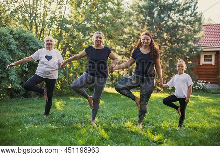 Blissful Females Of Four Generations Of One Family Standing On One Leg Holding Each Other Hands Warm