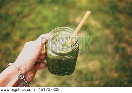 woman's hand holding a jar with green cold-pressed juice, nature background. Healthy eating, detoxing, juicing, body cleancing concept