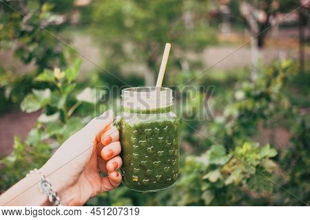woman's hand holding a jar with green cold-pressed juice, nature background. Healthy eating, detoxing, juicing, body cleancing concept