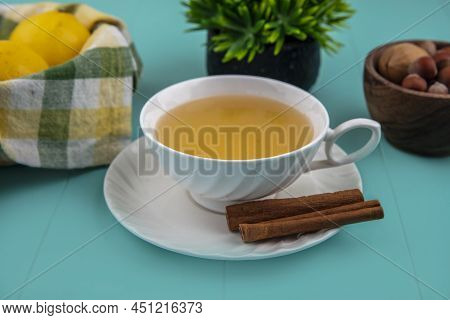 Side View Of Cup Of Hot Toddy With Cinnamon On Saucer And Lemons With Nuts On Blue Background